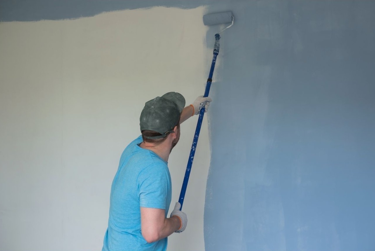 Painter applying paint to an interior wall with an extension roller